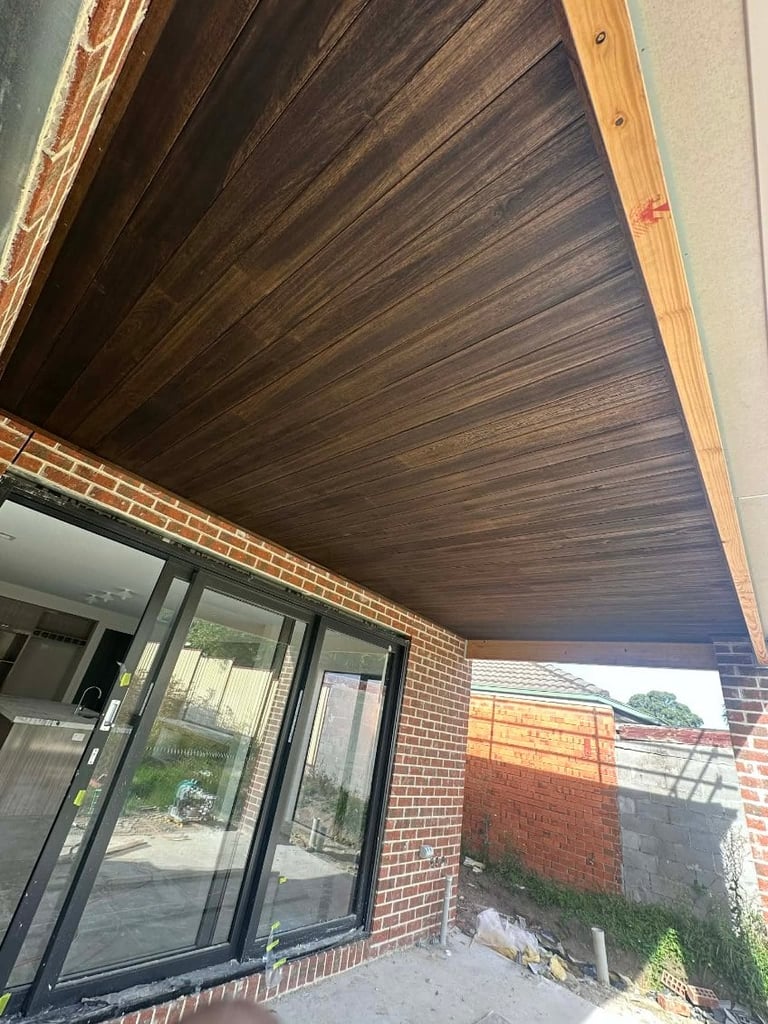 Modern covered patio with dark wood ceiling and light brick walls, featuring glass sliding doors and open view to backyard