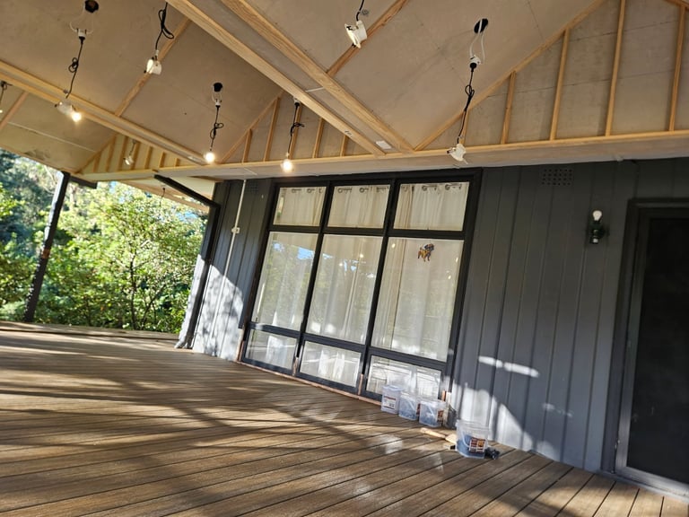 Empty covered outdoor deck with wooden flooring, metal walls, exposed wood beams, and large glass sliding doors with natural lighting