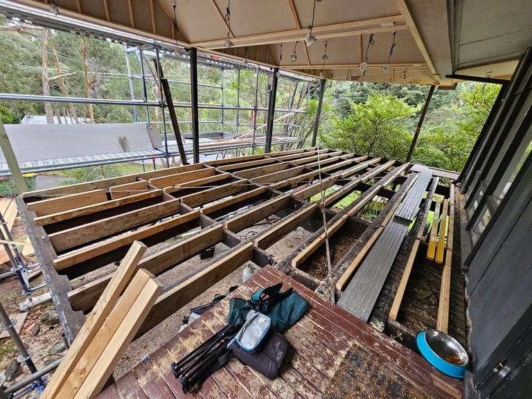 Interior construction of a covered structure showing wooden framing beams and metal railings under a canvas canopy roof